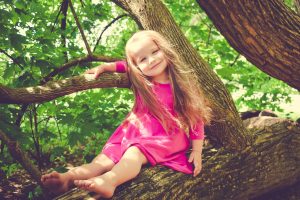 Happy girl sitting in tree, waring a pink dress