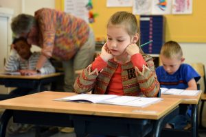 School girl sitting at classroom desk, looking at work