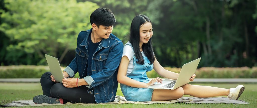 Boy and girl sitting with backs to each other with laptops