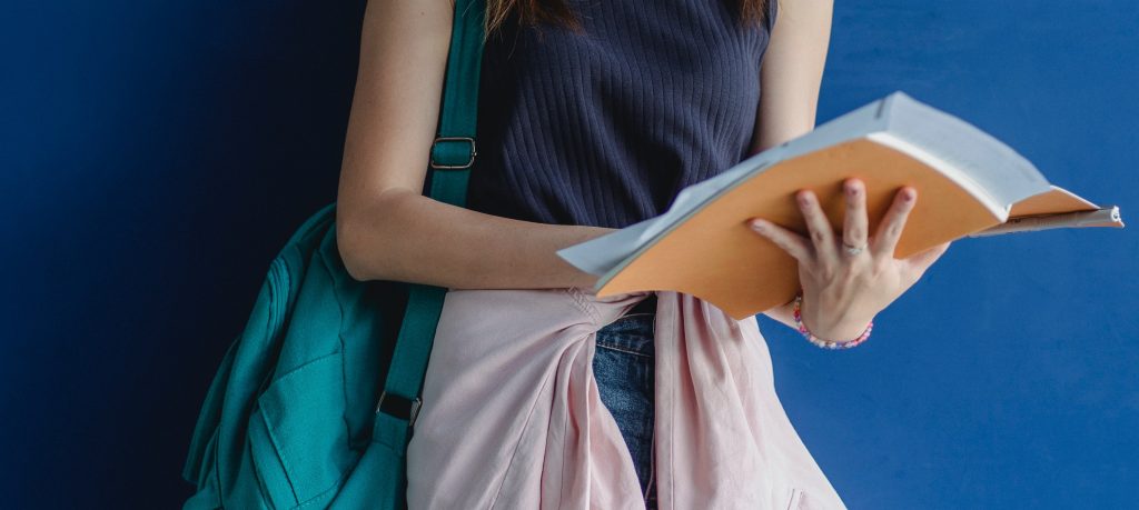 Woman holding book with backpack on shoulder