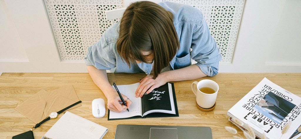 Woman writing notes in notebook in front of laptop