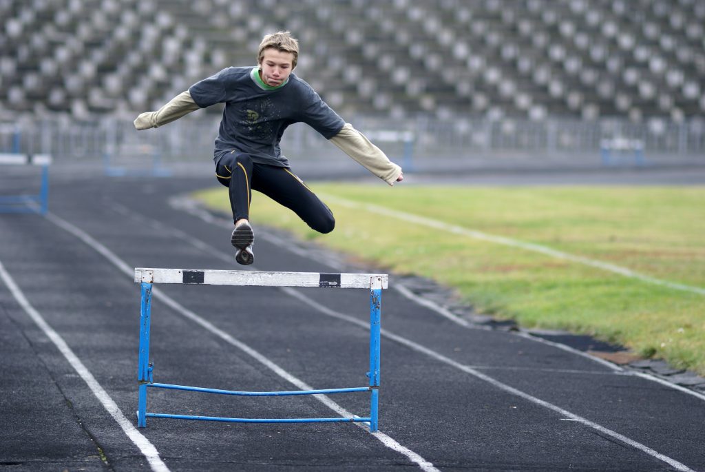 Man jumping over hurdle on running track.