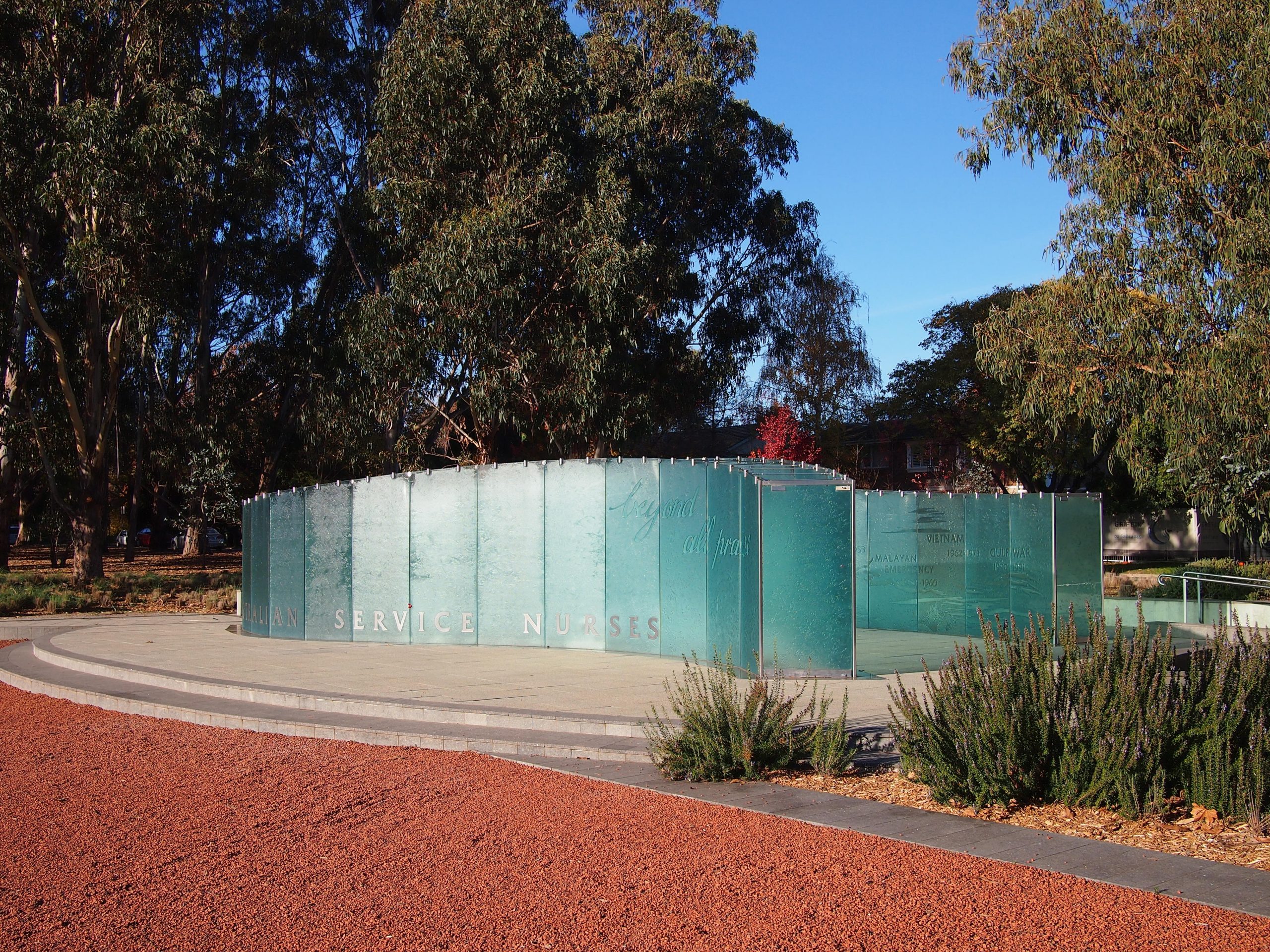 Photo of the Australian Service Nurses National Memorial which looks like a curved wall of glass surrounded by the red Australian dirt