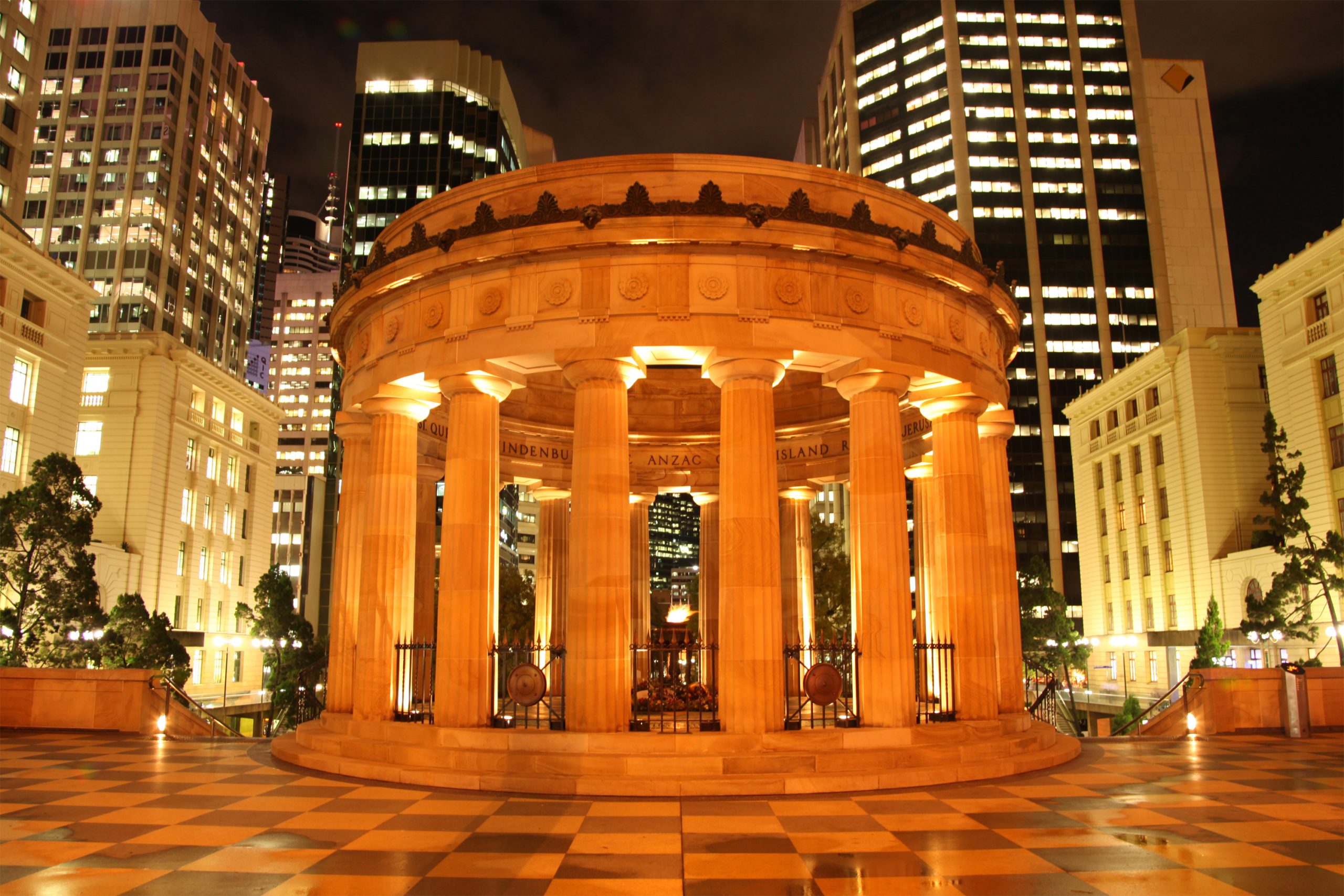 ANZAC Shrine of Remembrance at night, surrounded by an orange glow and Brisbane buildings.