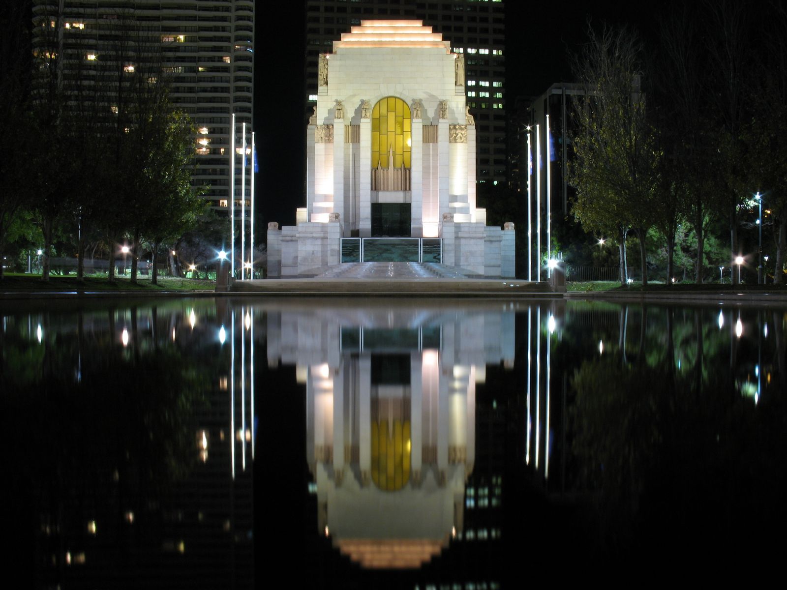 The ANZAC War Memorial in Sydney at night. It's white building that sits in front of a lake and the building reflection appears in the water,