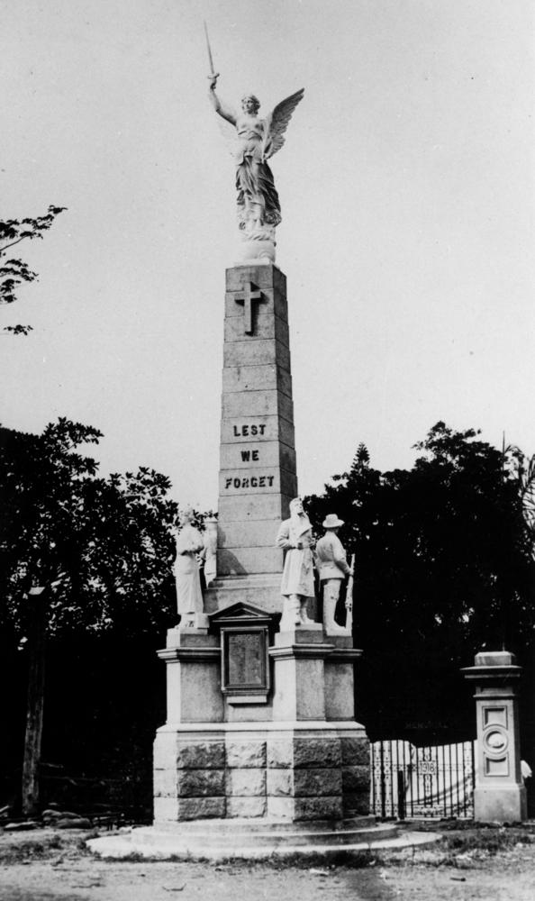 Old black and white photo of people standing on a statue with an angel holding a sword with the words 'lest we forget'