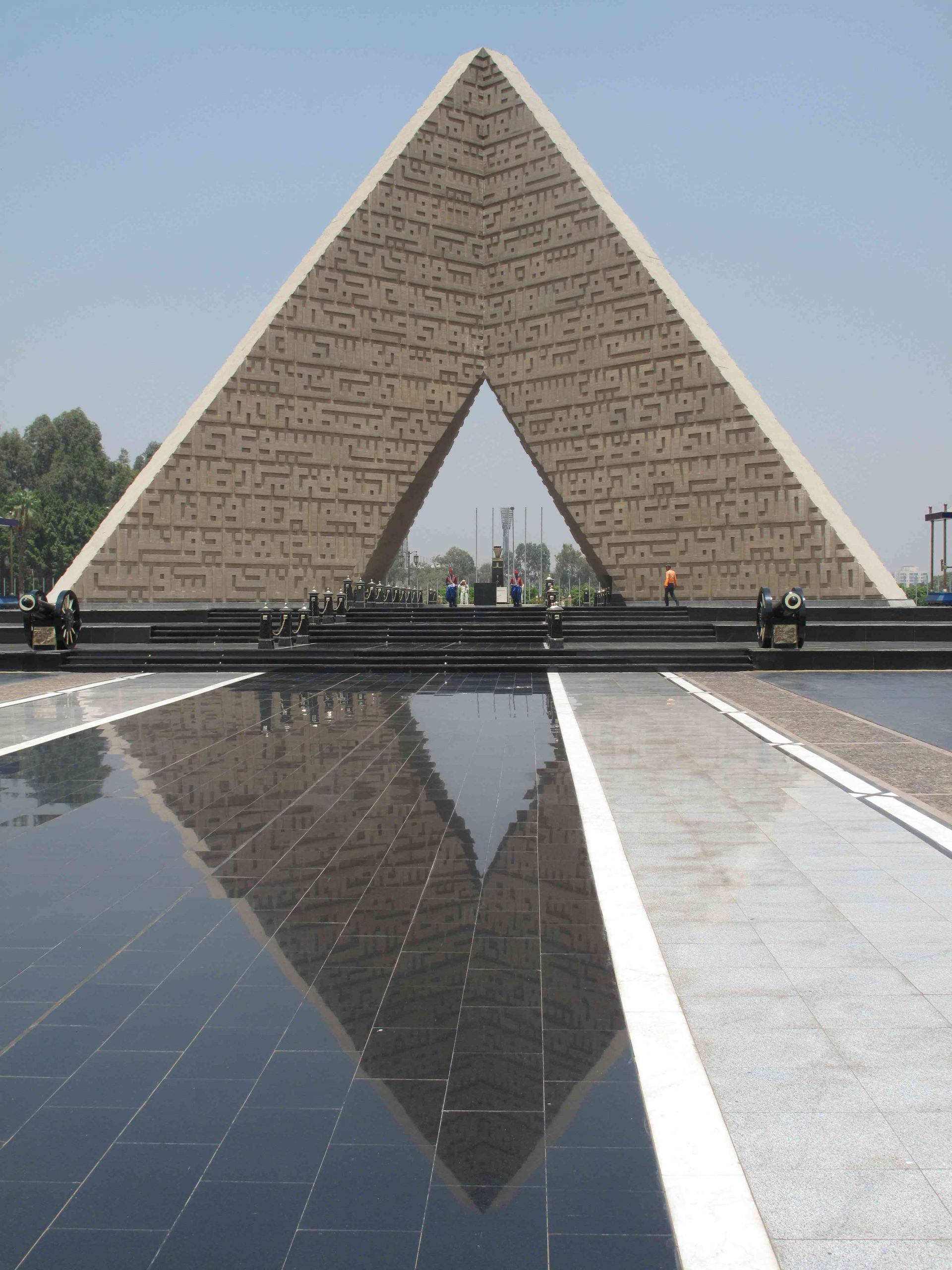 A giant monument in the shape of a triangle with people standing around it and beneath its arch