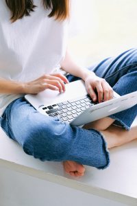 Woman wearing white shirt and jeans with laptop on lap