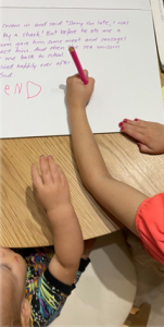 Child writing her name with red felt-tip pen at bottom of white paper