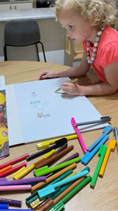 coloured pens on a desk with child drawing on white paper