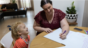 child smiling while woman writes on paper