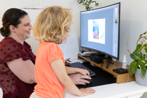 woman and child touching mouse while looking at computer monitor