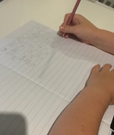 child's hand holding pencil and writing on lined paper