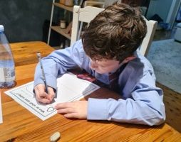 Boy sitting at table writing with pen and paper