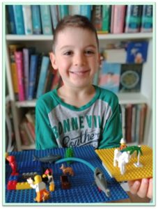 boy in front of bookshelf smiling at camera while displaying lego models of underwater scenes