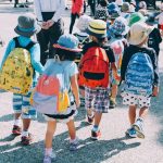 School children walking and holding hands, wearing bucket hats and colourful backpacks