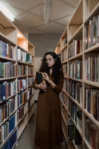 A photo of a woman standing in a library holding a book