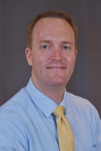 Dr Douglas Ellison is a white male with reddish-brown hair dressed in a blue shirt with a gold tie.