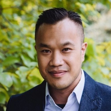 Man with short black hair, wearing an open collar white shirt and blue jacket