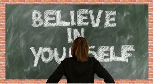 A decorative image of a person looking at a blackboard. The words 'believe in yourself' are written on the board.