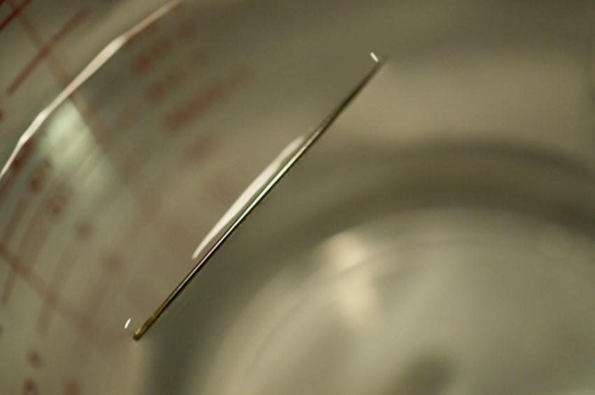 The weight of a needle on top of water pulls the surface tension downward; at the same time, the surface tension of the water is pulling it up, suspending the needle on the surface of the water and keeping it from sinking.